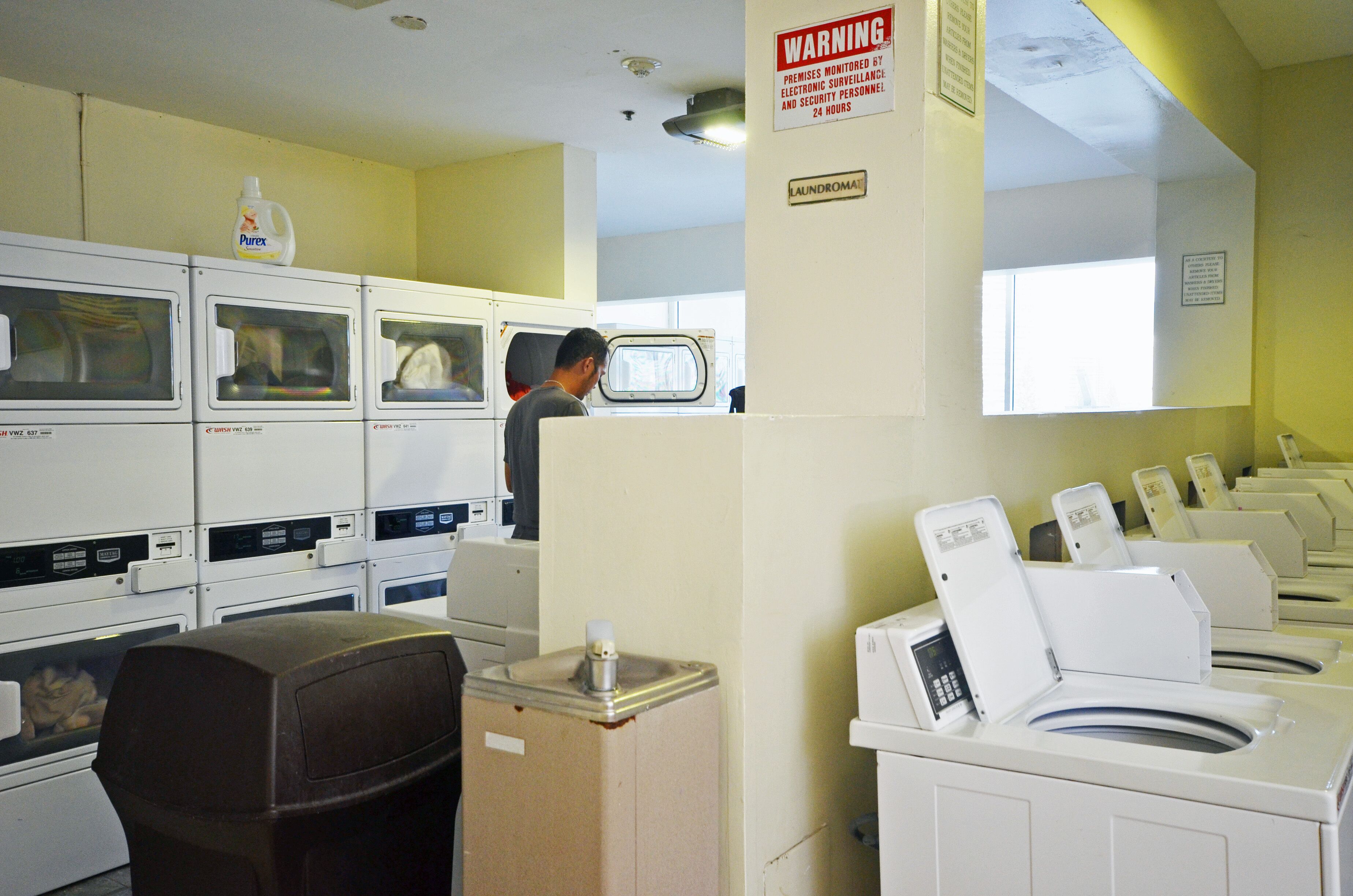 A laundromat with multiple washing machines and dryers, a warning sign, and a man operating one of the machines.
