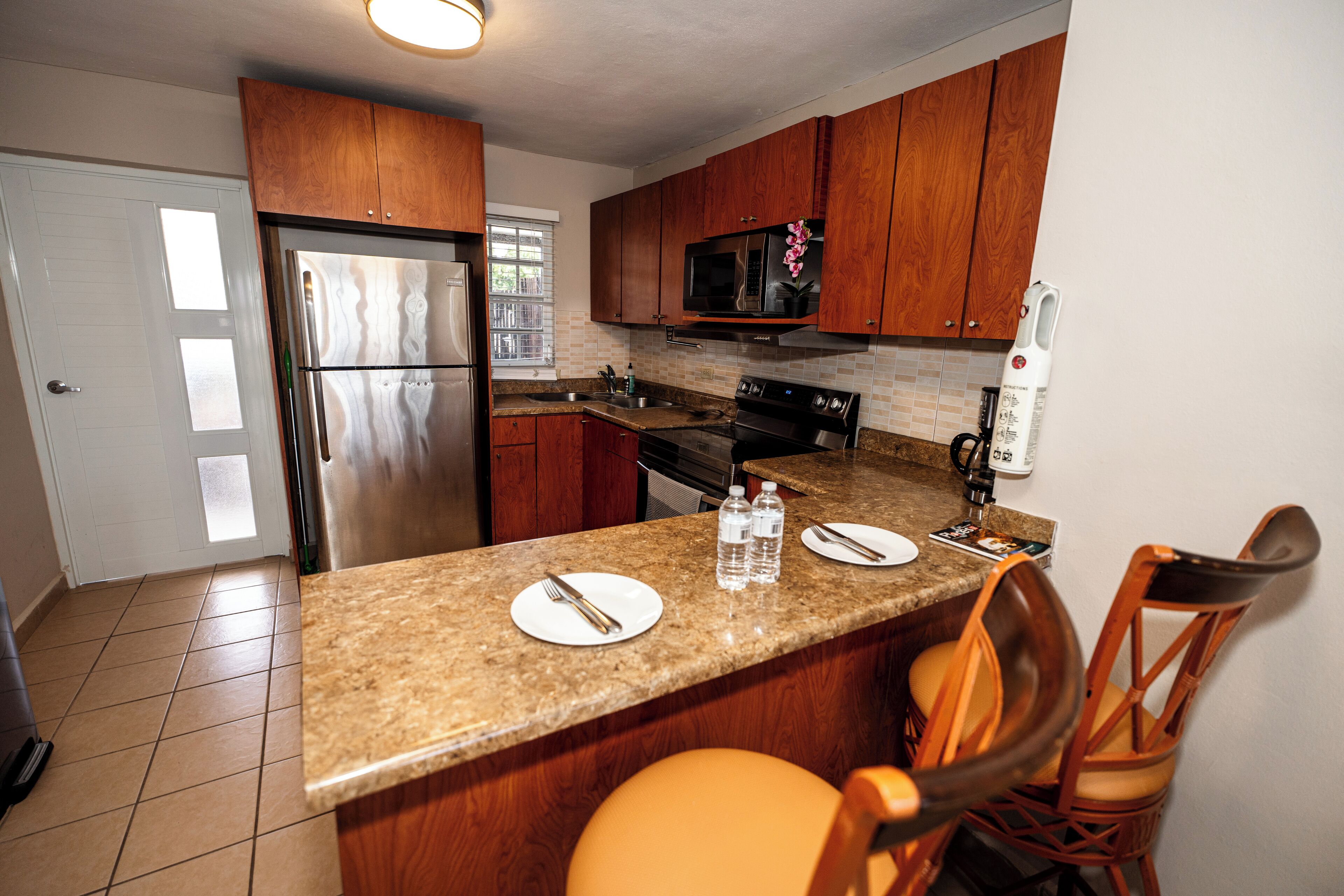 A kitchen with wooden cabinets, a stainless steel refrigerator, a microwave, and a granite countertop.