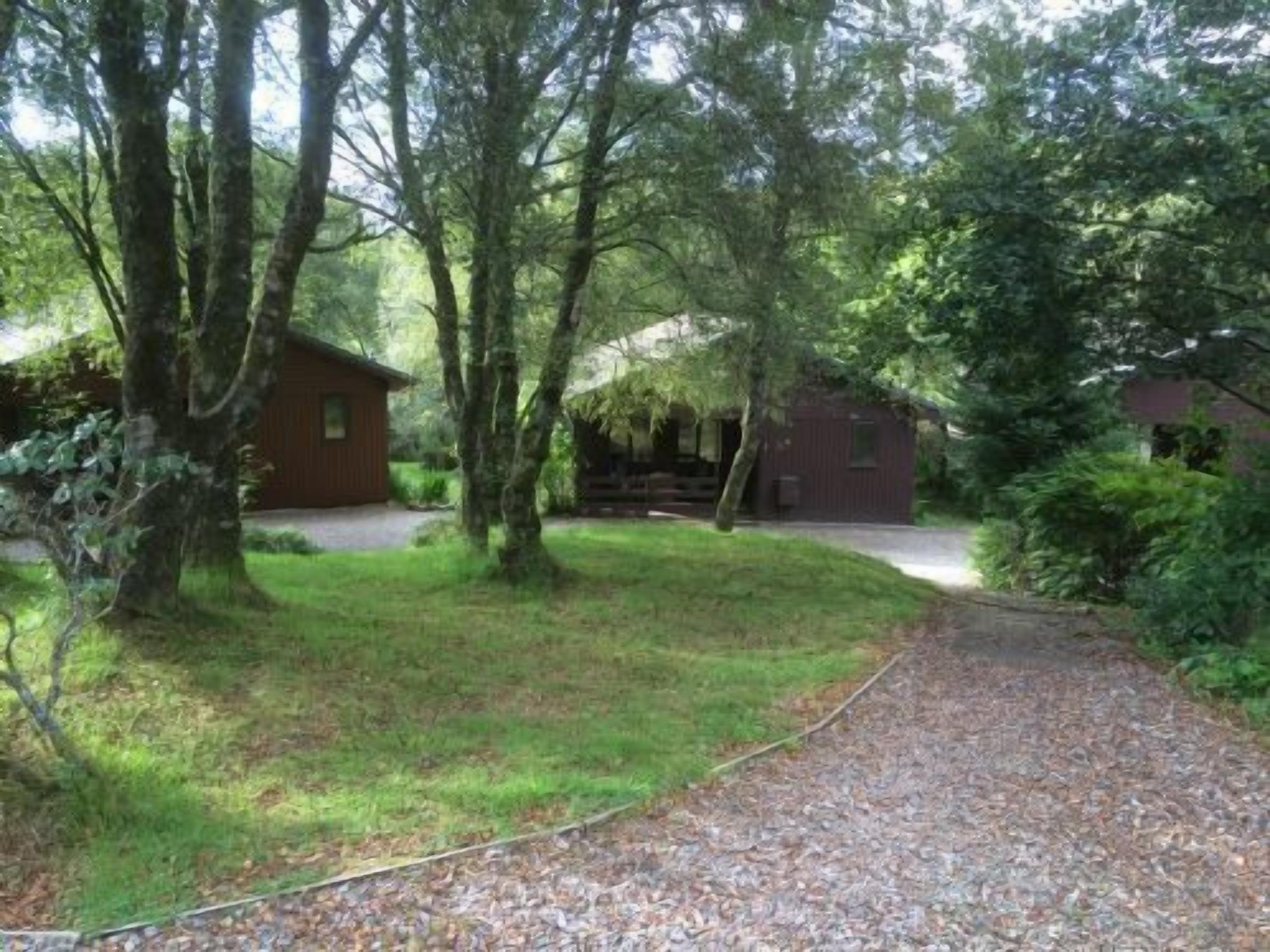 Un sentier de gravier mène à un chalet en bois entouré d’arbres.