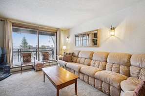 A living room with a sofa, a coffee table, a TV, and a balcony with a view.