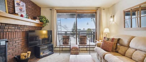 A living room with a fireplace, a sofa, a TV, and a balcony with a view.