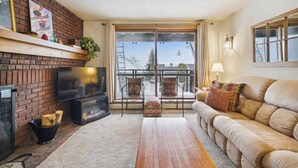 A cozy living room with a fireplace, a sofa, and a balcony with a view. - Ski on/ski off, conveniently located with beautiful views, Sunrise B3 (Killington)