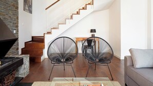 Ein modernes Wohnzimmer mit Kamin, zwei schwarzen Stuhlgestellen, einer Couch und einer Treppe.