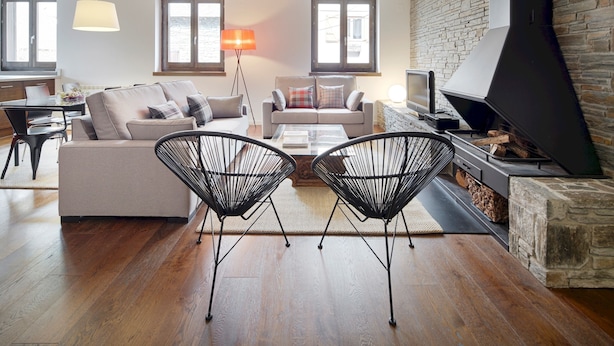 Ein modernes Wohnzimmer mit einer Couch, zwei schwarzen Stuhlgestellen, einem Couchtisch, einem Fernseher und einem Kamin.