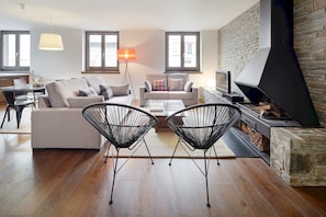 Una sala de estar moderna con un sofá, dos sillas de alambre negras, una mesa de centro, un televisor y una chimenea.