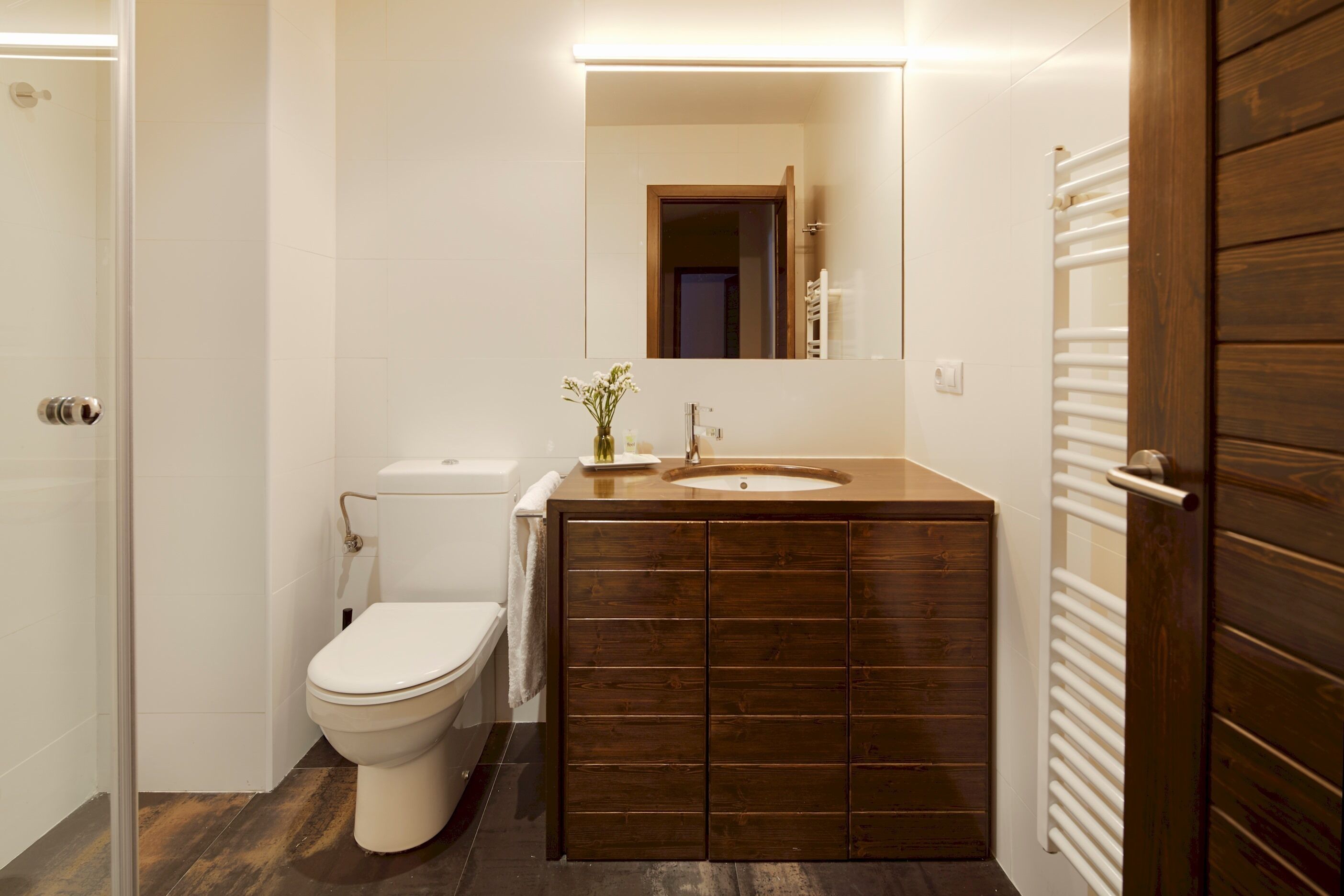 A bathroom with a wooden vanity, a white toilet, and a mirror above the sink.