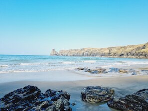 Una playa con formaciones rocosas y acantilados al fondo.