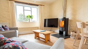 A cozy living room with a sofa, a wooden coffee table, a TV, and a wood-burning stove. - 4* self catering, farm stay cottage. Sleeps 4 (Boscastle)
