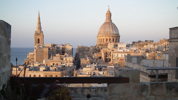 A terrace with a table set for dining, overlooking a cityscape with historic buildings and a large dome structure. - Spacious Apartment- historical character- fascinating views over old town & sea (Valletta)