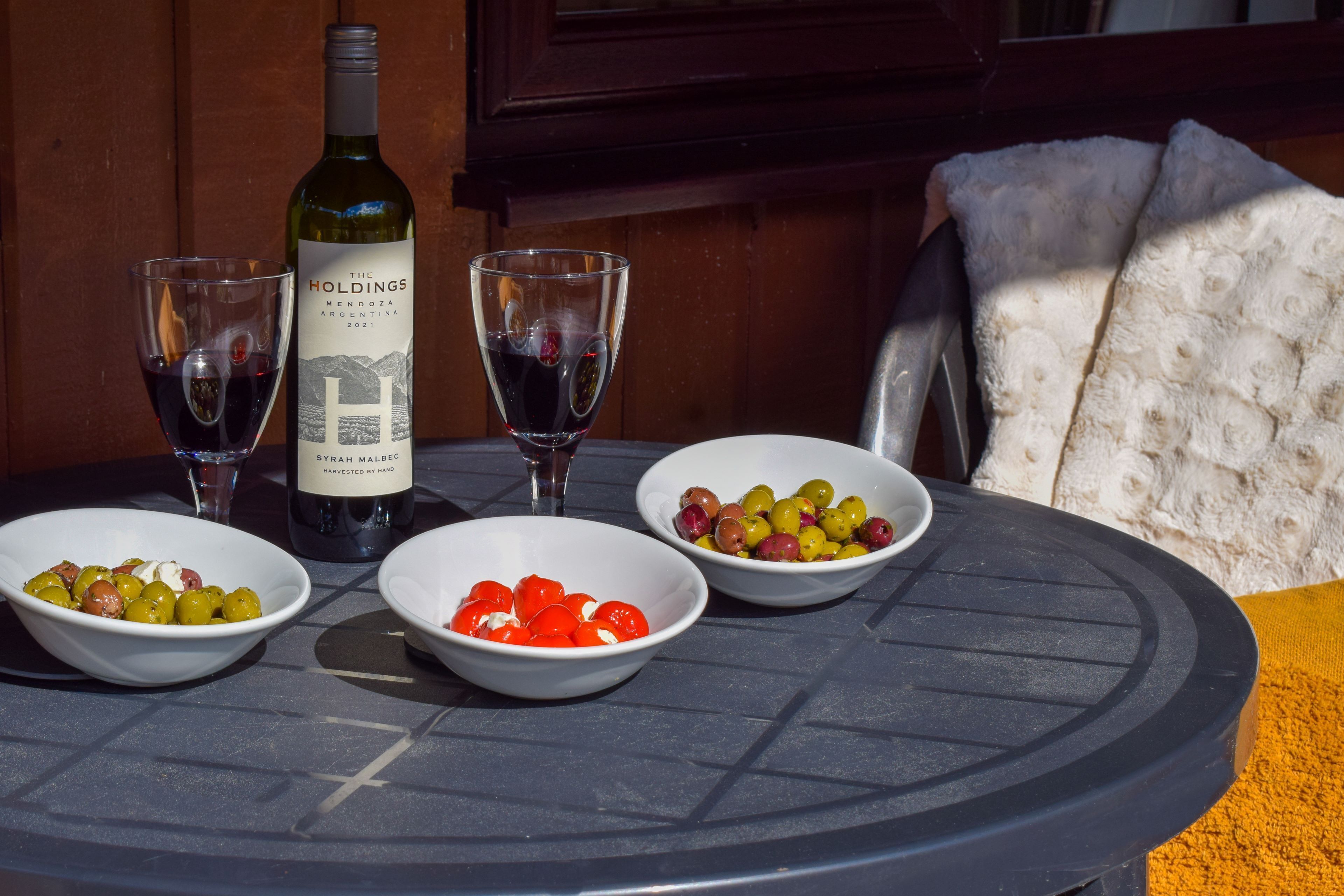 A table with a wine bottle, two glasses of red wine, and three bowls of olives.