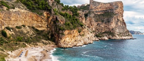 A coastal landscape with a prominent rocky cliff and a beach with umbrellas.
