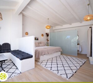 Un dormitorio moderno y bien iluminado, con cama, zona de estar y un ventanal grande.
