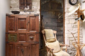 A rustic room with a wooden cabinet, a chair with a patterned throw, and a wall-mounted clock.