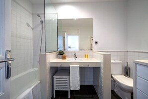 Ein Badezimmer mit Duschkabine aus Glas, einem weißen Waschbecken mit Spiegel darüber und einer Toilette.