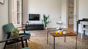 A modern living room with a flat-screen TV, a dining area with a table set for breakfast, and a large window with a view of the outside. - Barcelona Balconies 4 - Habitat Apartments (Barcelona)