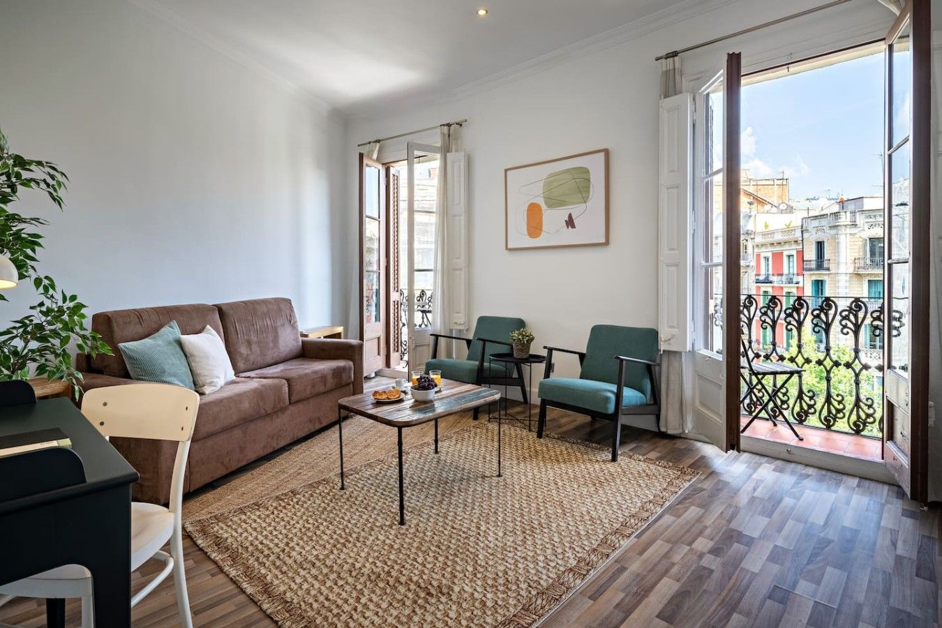 A living room with a brown sofa, a coffee table, and two chairs. There is a large window with a view of buildings outside.