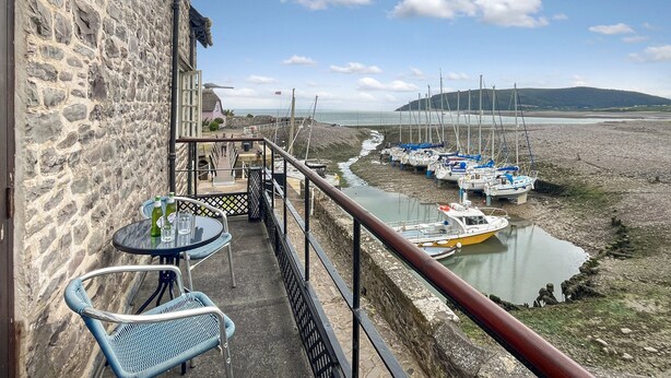 A balcony with stone walls, a table with chairs, and a view of boats on a waterway.