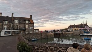 A waterfront scene with stone buildings, a dock with boats, and a crowd of people.