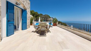 Un balcon avec une table et des chaises, une plante en pot et une vue sur la mer.