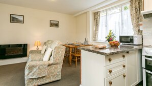 A cozy living room with a sofa, a fireplace, and a dining area with a table and chairs. - Four star two bedroom cottage both with en suite facilities (Minehead)