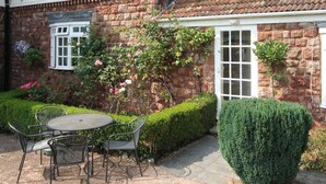 A house with a garden patio, a white exterior, and a brick facade. - Four star two bedroom cottage both with en suite facilities (Minehead)
