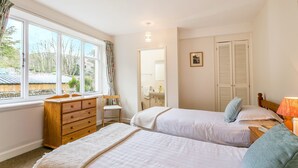 A bedroom with two beds, a dresser, a window with curtains, a mirror, a bedside table with a lamp, and a door with shutters. - Four star two bedroom cottage both with en suite facilities (Minehead)