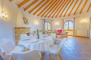 A dining area with a stone fireplace, wooden beams, and a table set for six.