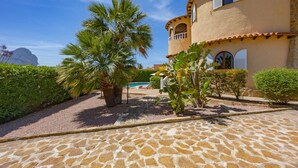 Un edificio con un patio empedrado de piedra, palmeras y una piscina al fondo.