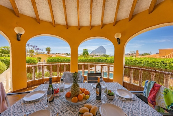A dining area with a table set for two, a pineapple, oranges, and a bottle of wine.