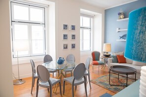 A modern living room with a glass dining table, grey chairs, a blue sofa, and a patterned rug. - RENT4REST LISBON DOWNTOWN DESIGNER'S APARTMENT (Lisboa ciudad)
