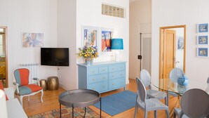 Een moderne woonkamer met een flatscreen televisie, een blauwe kast, een eettafel met stoelen en een kleine ronde tafel.