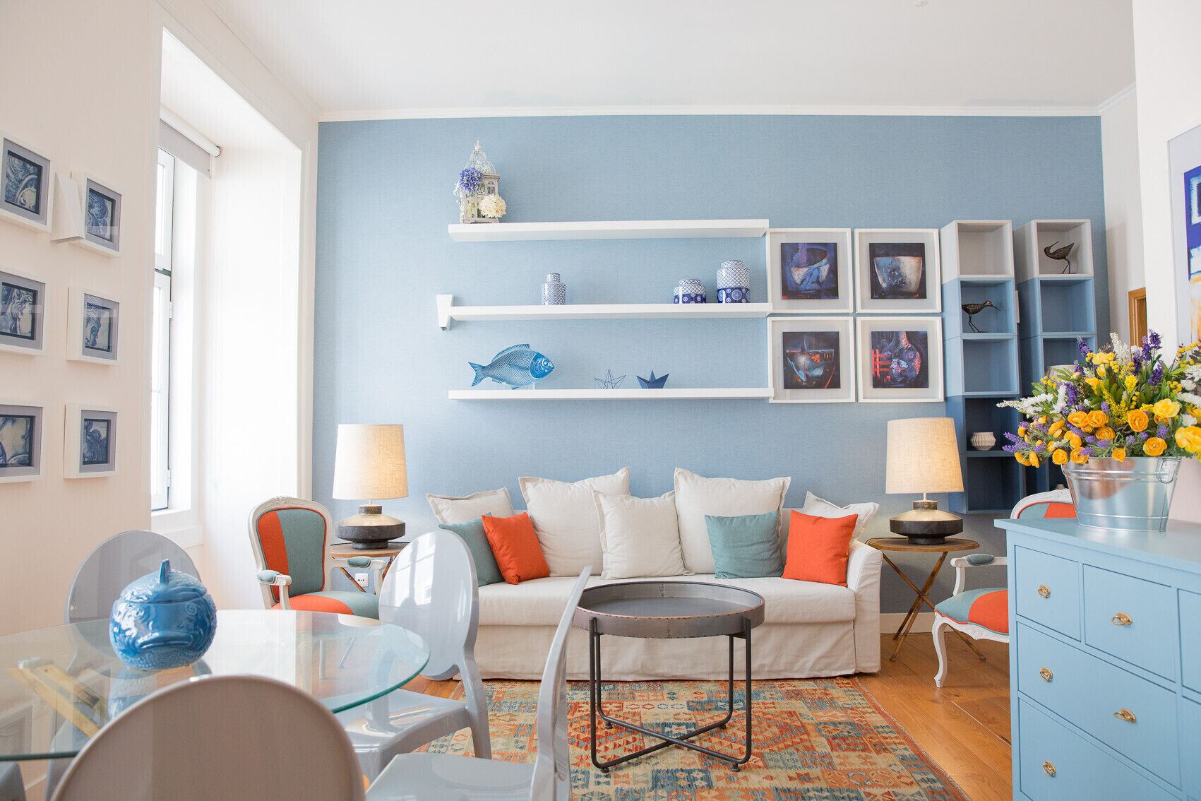 Una sala de estar con pared azul, sofá blanco y estanterías decorativas.