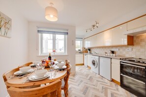 A modern kitchen with a dining area, featuring a wooden table set for a meal, a washing machine, and a stove.
