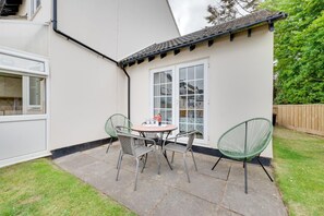 A patio with a round table and four chairs, a white door, and a small garden area. - 2 Bed in Instow (oc-n1093) (Instow)