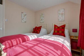 A bedroom with two beds, each with a red and white checkered pillow, and a small bedside table with a lamp.