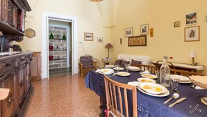 A dining room with a table set for four, a wicker chair, a sofa, and a wooden cabinet.
