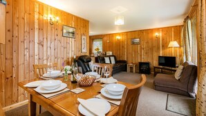 A wooden-paneled room with a dining table set for four, a sofa, a television, and a fireplace. - Four star Lodge with two bedrooms, fabulous views yet close to pubs and beach (Minehead)