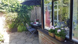 An outdoor patio with a table and chairs, surrounded by lush greenery and potted plants. - Portrush - Hope Cottage - sleeps 5 guests  in 3 bedrooms (Portrush)