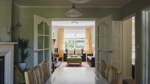 A dining room with a long table, chairs, a chandelier, and a view through a doorway to another room with a sofa and curtains. - Portrush - Hope Cottage - sleeps 5 guests  in 3 bedrooms (Portrush)