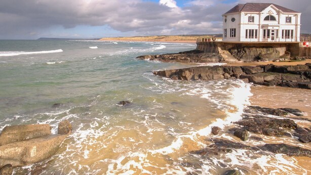 A coastal building with a white facade and a grey roof, situated on a rocky shoreline with waves crashing onto the rocks. - Portrush - Hope Cottage - sleeps 5 guests  in 3 bedrooms (Portrush)