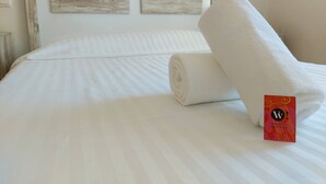 Una cama bien tendida con sábanas blancas y una toalla enrollada.