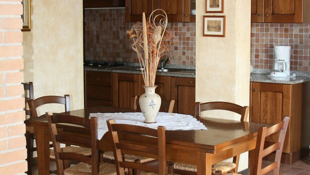 Un coin repas avec une table et des chaises en bois, un vase contenant des plantes séchées et des lampes suspendues.