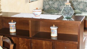 Une table de salle à manger en bois, recouverte d’une nappe à motifs floraux, un banc en bois et une commode à tiroirs.