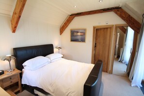 A bedroom with a bed, bedside tables, a wooden ceiling, and a door leading to another room. - The Stable Block, Porlock Weir (Porlock Weir)