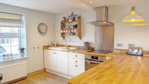 Een moderne keuken met een houten aanrecht, een inbouwoven en een groot raam met zonwering.