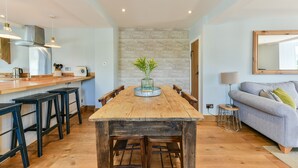 Een eethoek met een houten tafel, zwarte barkrukken en een vaas met groene planten.