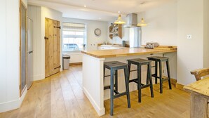 Een moderne keuken met een centraal eiland, barkrukken, een klok en een raam met uitzicht.