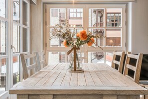 A wooden dining table with chairs, a vase with flowers, and large windows with a view of buildings. - Val de Ruda Luxe 33 by FeelFree Rentals (Baqueira)
