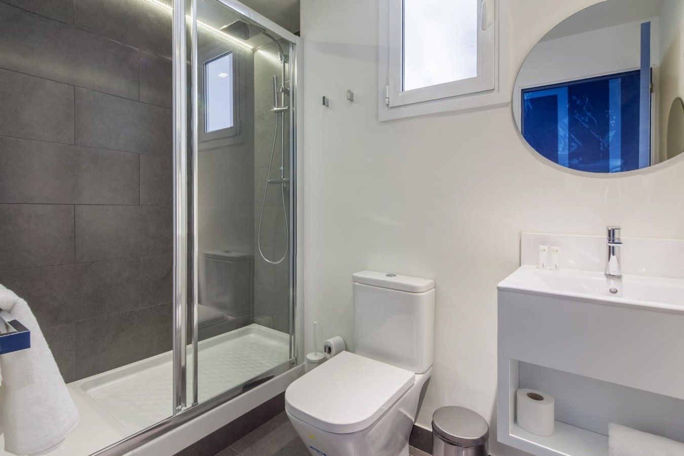 A modern bathroom with a glass-enclosed shower, a white toilet, and a sink with a mirror above it.