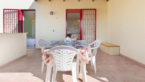A covered patio with a table set for dining, white chairs, and a small bench. - Appartamento Oasi by BarbarHouse (Torre Pali)